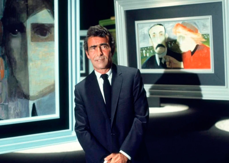 Hombre adulto de pie entre cuadros en una galería de arte.