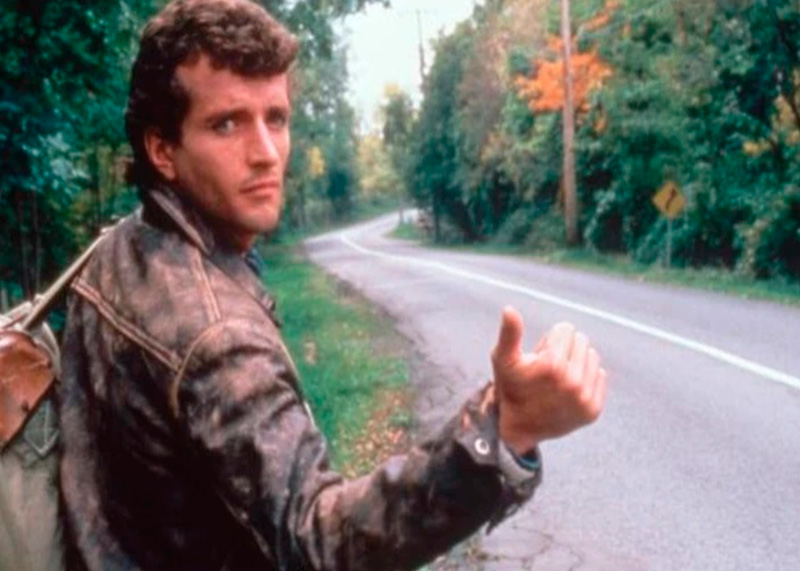 Hombre pidiendo aventón en una ruta desolada dentro del bosque.