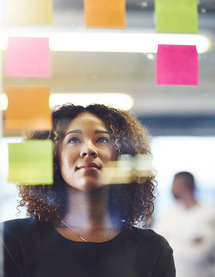 Woman looking at a blackboard with sticky notes and analyzing solutions.